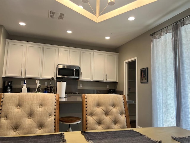 kitchen with stainless steel microwave, recessed lighting, visible vents, and white cabinets