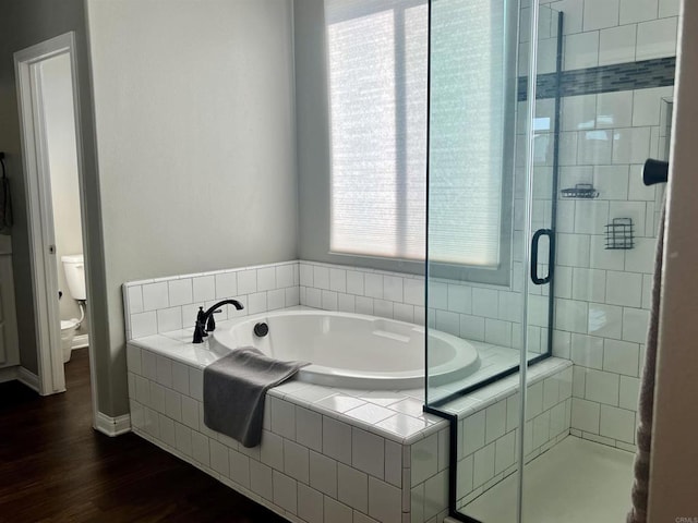 bathroom featuring a garden tub, a shower stall, toilet, and wood finished floors