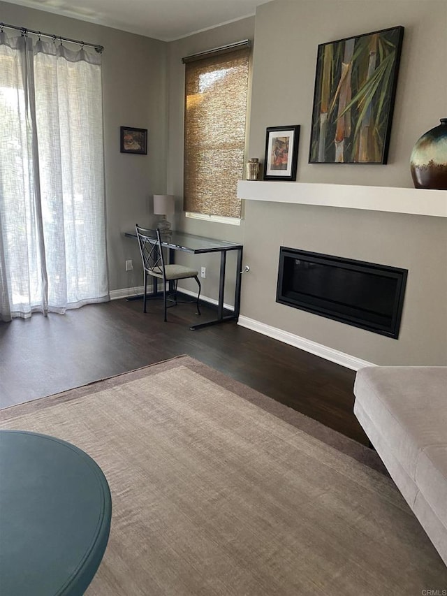 office featuring baseboards, wood finished floors, a glass covered fireplace, and a healthy amount of sunlight