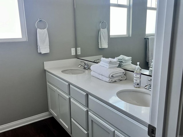 bathroom with double vanity, baseboards, a sink, and wood finished floors