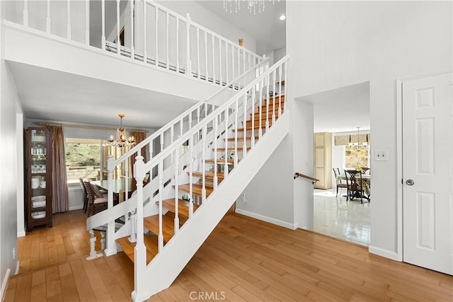 stairs with baseboards, a towering ceiling, hardwood / wood-style flooring, and a notable chandelier