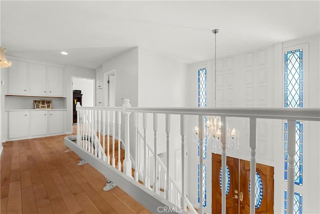 hallway with light wood-style floors, recessed lighting, a chandelier, and an upstairs landing