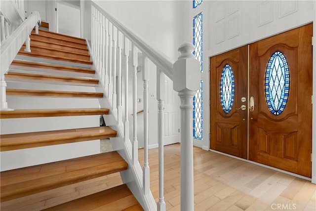 foyer entrance featuring a towering ceiling, light wood-style floors, baseboards, and stairway