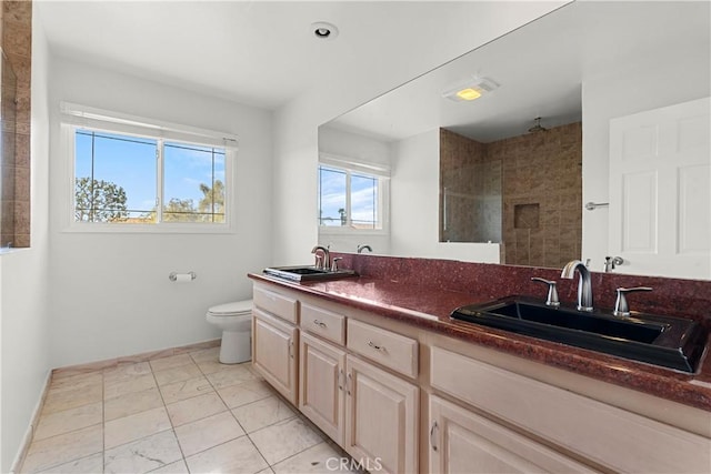 bathroom with double vanity, tiled shower, a sink, and toilet