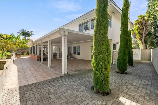 back of house featuring stucco siding, a sunroom, a gate, a patio area, and a fenced backyard