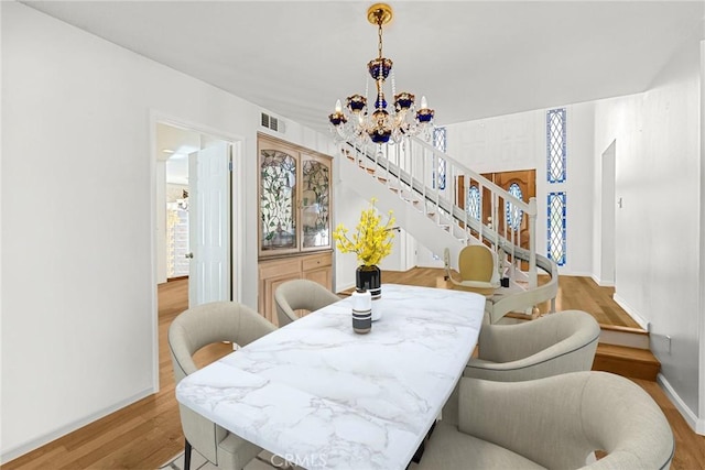 dining space with visible vents, stairway, wood finished floors, a chandelier, and baseboards