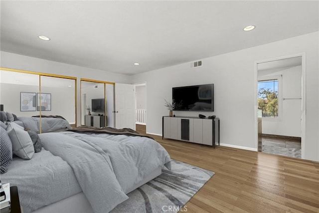 bedroom with recessed lighting, wood finished floors, visible vents, baseboards, and multiple closets