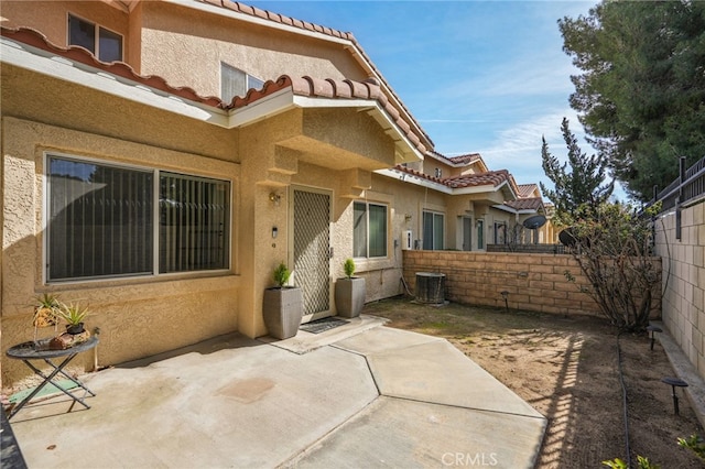 view of exterior entry featuring a patio area, a tile roof, fence, and stucco siding