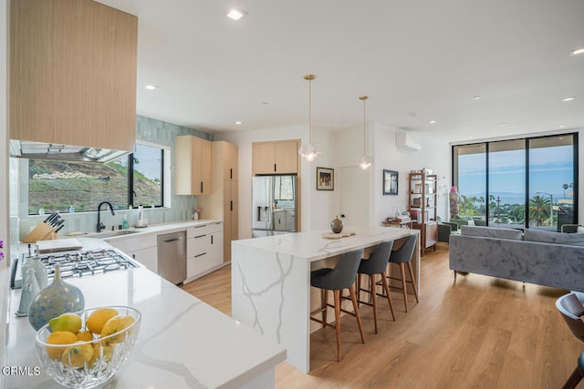 kitchen featuring a center island, a wall unit AC, stainless steel appliances, light wood-style flooring, and a sink