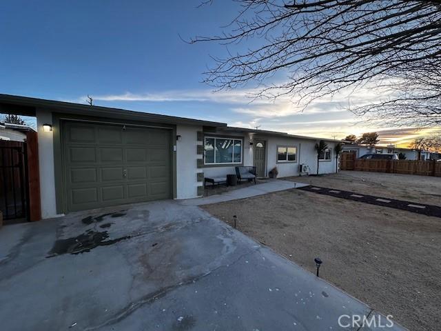 ranch-style house featuring a garage, driveway, fence, and stucco siding