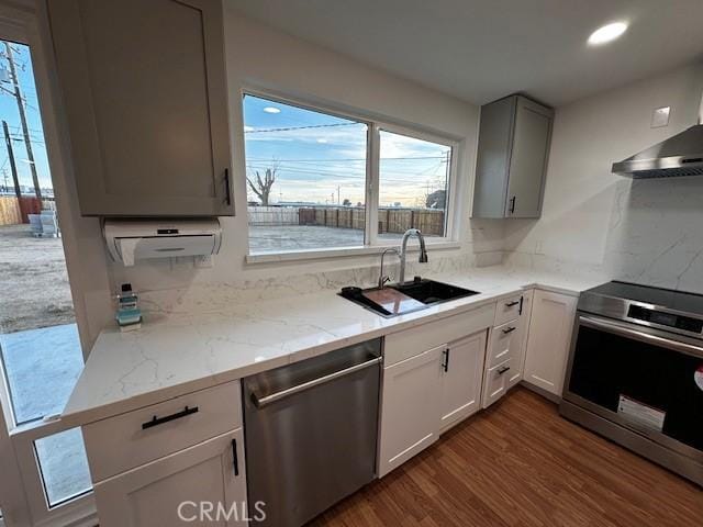 kitchen with stainless steel appliances, light stone counters, dark wood-style flooring, and a sink