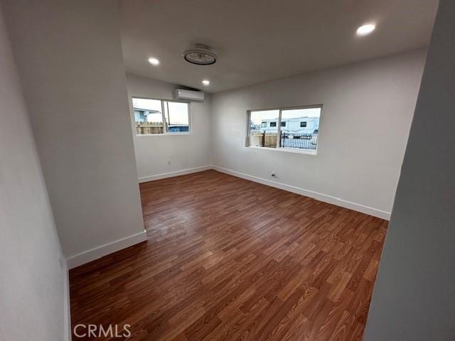 empty room featuring an AC wall unit, recessed lighting, dark wood finished floors, and baseboards