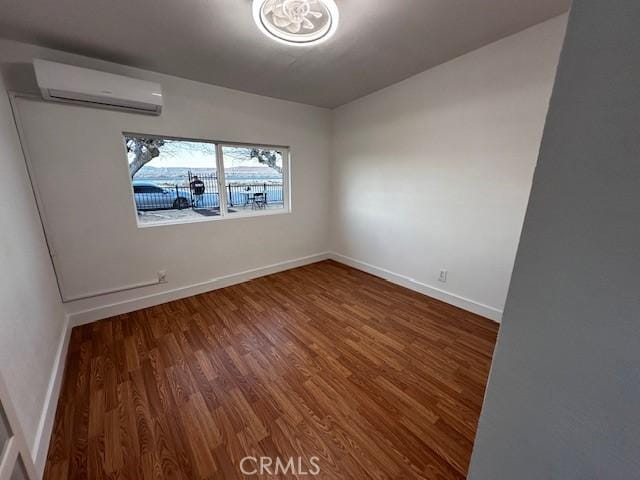 empty room featuring an AC wall unit, wood finished floors, and baseboards