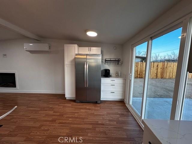 kitchen with light stone counters, a wall unit AC, dark wood-style flooring, white cabinetry, and freestanding refrigerator