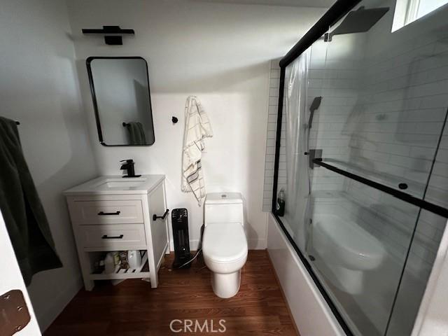 full bathroom featuring baseboards, toilet, enclosed tub / shower combo, wood finished floors, and vanity