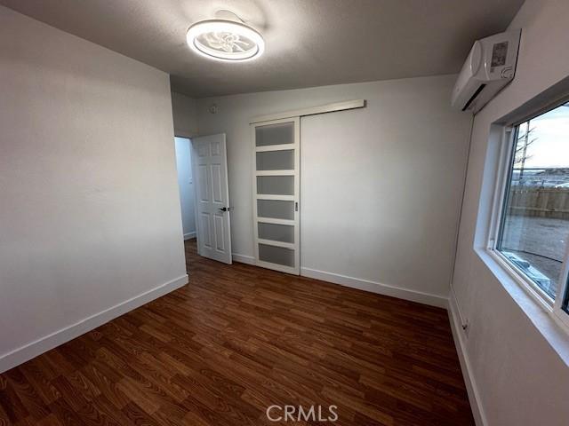 unfurnished bedroom with a closet, a wall mounted air conditioner, wood finished floors, and baseboards