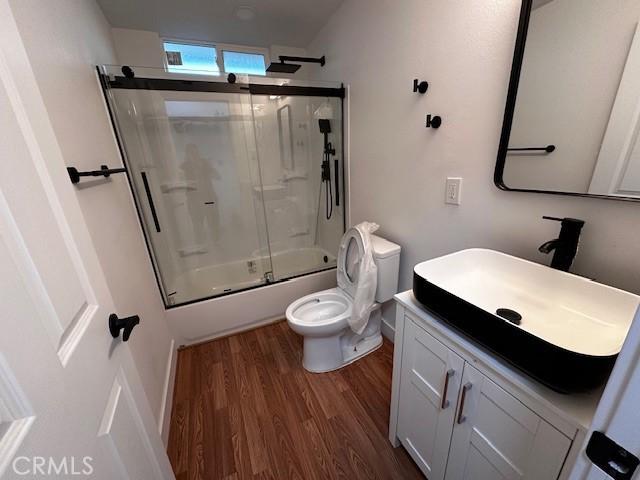 full bathroom with bath / shower combo with glass door, vanity, wood finished floors, and toilet