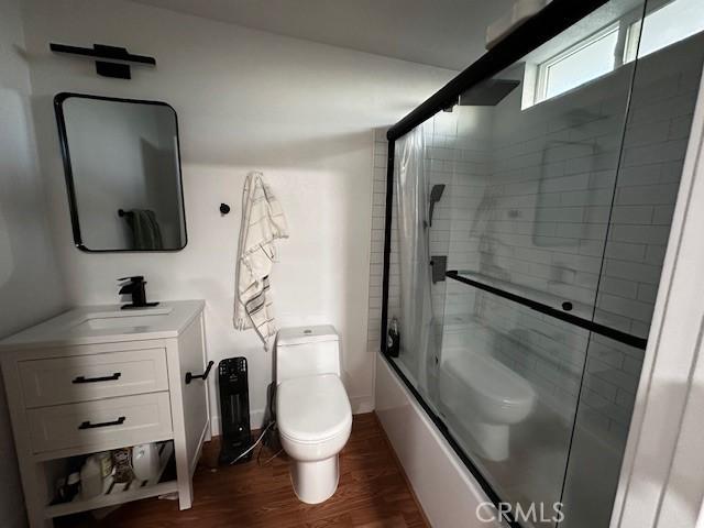 full bathroom with toilet, enclosed tub / shower combo, wood finished floors, and vanity