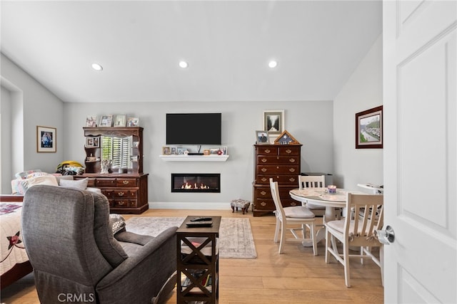 living area with light wood finished floors, recessed lighting, vaulted ceiling, and a glass covered fireplace