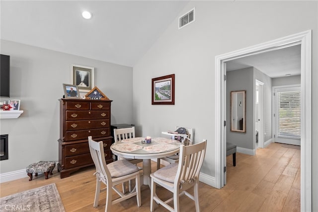 dining space featuring lofted ceiling, visible vents, light wood-style flooring, a glass covered fireplace, and baseboards