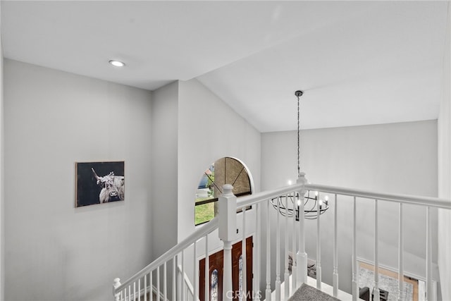 corridor featuring lofted ceiling, an upstairs landing, and an inviting chandelier