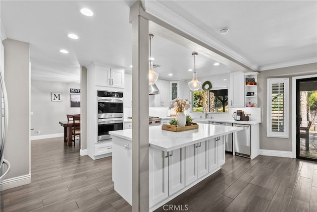 kitchen featuring dark wood-style flooring, crown molding, appliances with stainless steel finishes, white cabinetry, and a sink