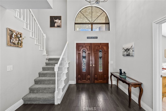 foyer entrance with a towering ceiling, dark wood-style floors, stairway, and baseboards