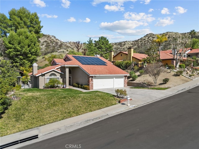 view of front of property with a garage, solar panels, concrete driveway, a mountain view, and a front lawn