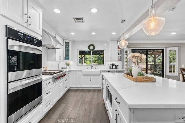 kitchen with visible vents, wall chimney exhaust hood, appliances with stainless steel finishes, a center island, and a sink