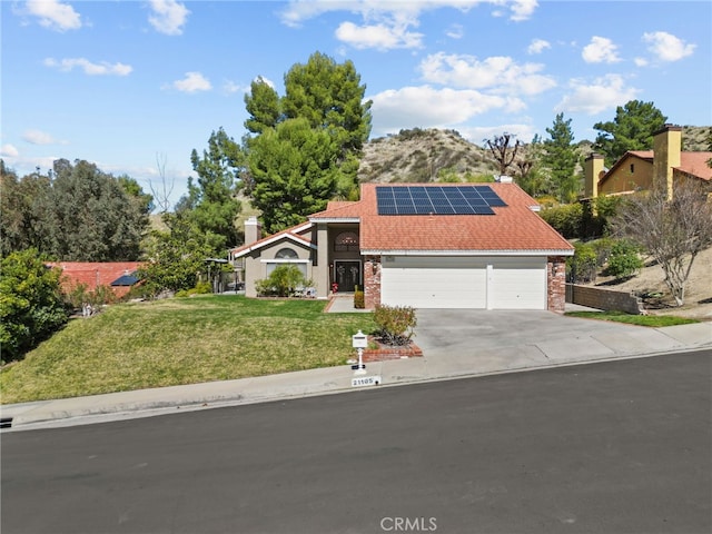 view of front of home with brick siding, solar panels, concrete driveway, an attached garage, and a front lawn