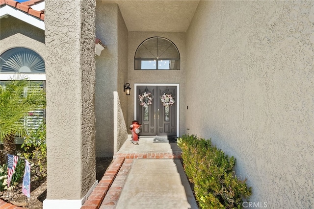 property entrance with a tiled roof, french doors, and stucco siding