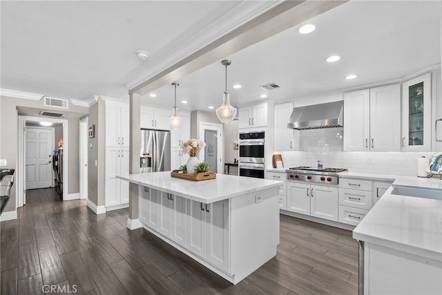 kitchen featuring visible vents, appliances with stainless steel finishes, a center island, wall chimney range hood, and a sink