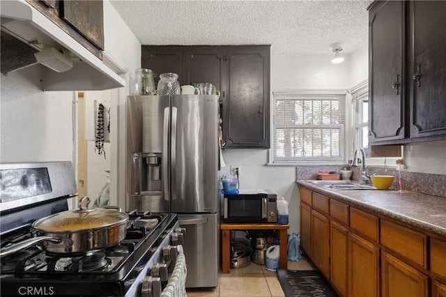 kitchen featuring light tile patterned floors, stainless steel fridge, gas range oven, under cabinet range hood, and a sink