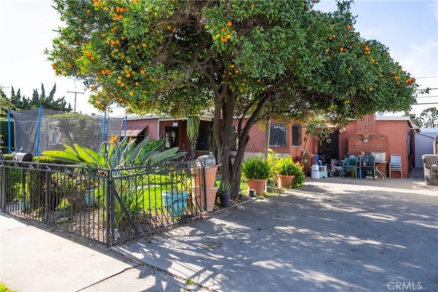 view of property hidden behind natural elements with a trampoline, fence, and stucco siding