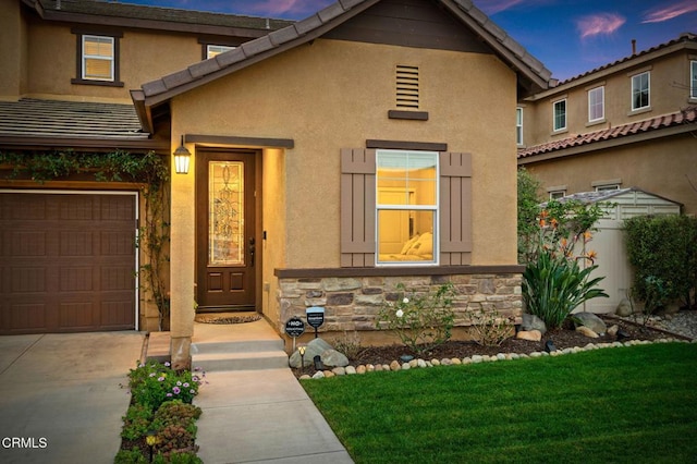 exterior entry at dusk with a garage, stone siding, and stucco siding