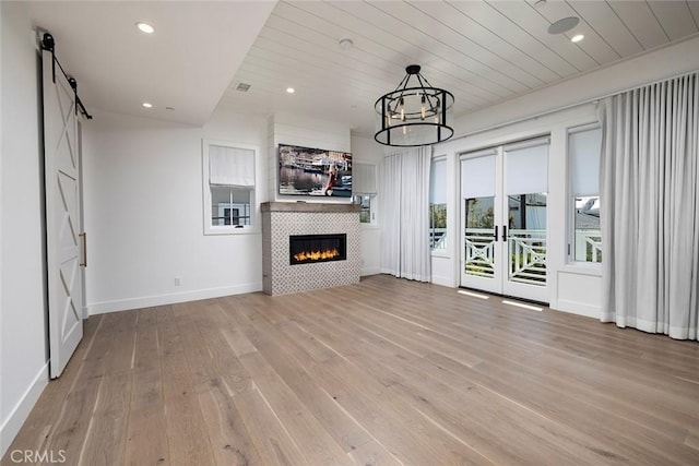 unfurnished living room with a barn door, baseboards, a tile fireplace, light wood-style floors, and recessed lighting