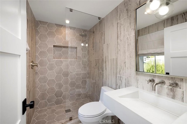 full bathroom featuring tile walls, tiled shower, toilet, backsplash, and a sink