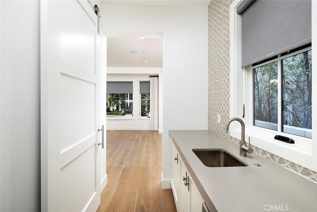 kitchen with light countertops, light wood-style flooring, a barn door, white cabinetry, and a sink