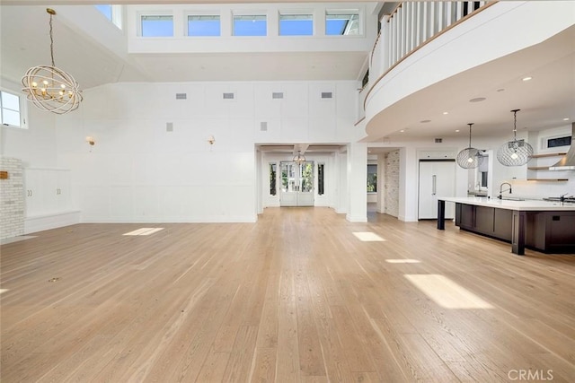 unfurnished living room featuring light wood-style flooring, a high ceiling, visible vents, and a sink