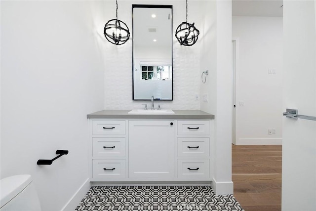 half bath featuring baseboards, toilet, wood finished floors, vanity, and a notable chandelier