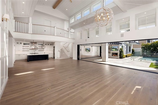 unfurnished living room with a notable chandelier, beam ceiling, stairway, and wood finished floors