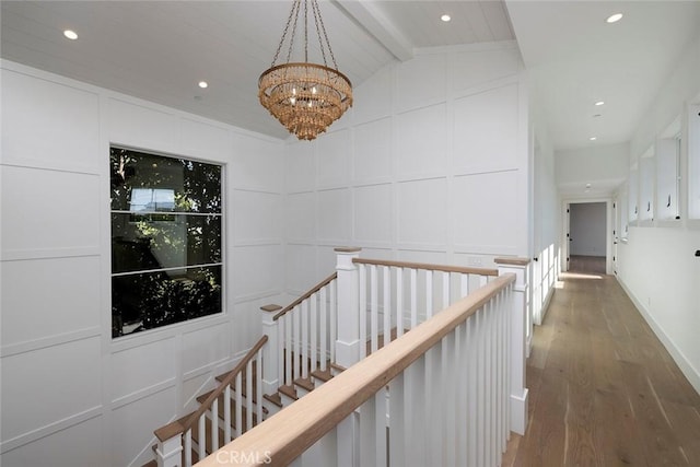 hallway featuring lofted ceiling with beams, recessed lighting, a decorative wall, wood finished floors, and an upstairs landing