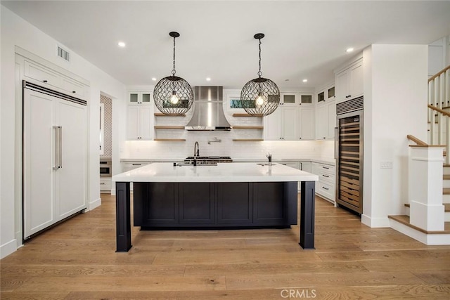 kitchen featuring paneled built in fridge, visible vents, light countertops, wall chimney range hood, and open shelves