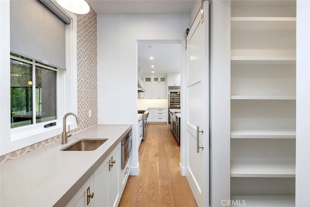 kitchen featuring light wood finished floors, a barn door, white cabinetry, open shelves, and a sink