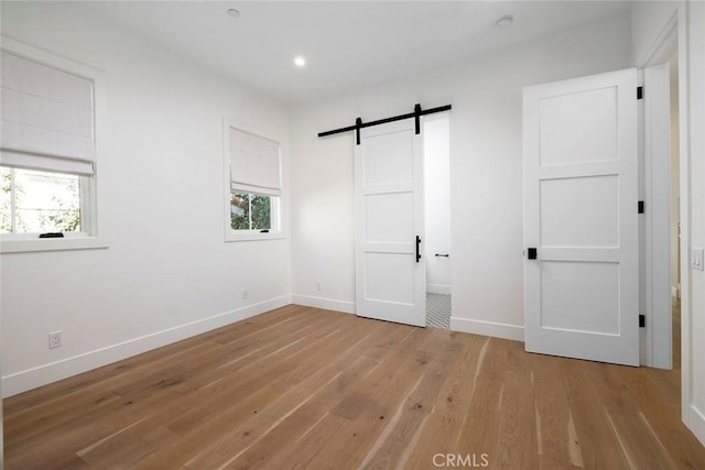 unfurnished bedroom with light wood finished floors, a barn door, multiple windows, and baseboards