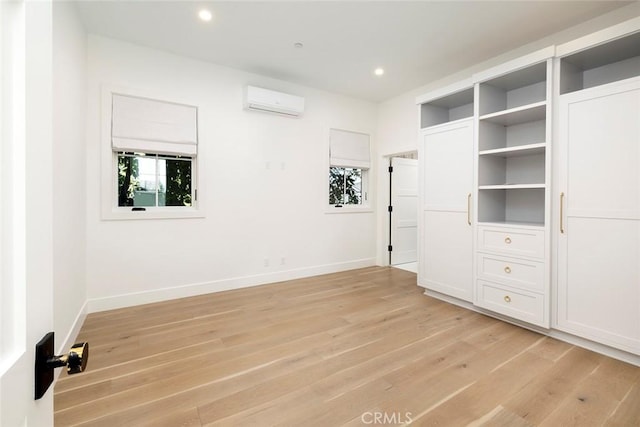 interior space with light wood finished floors, a wall mounted AC, and baseboards