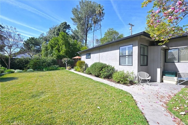 view of side of home with a patio area, stucco siding, and a yard