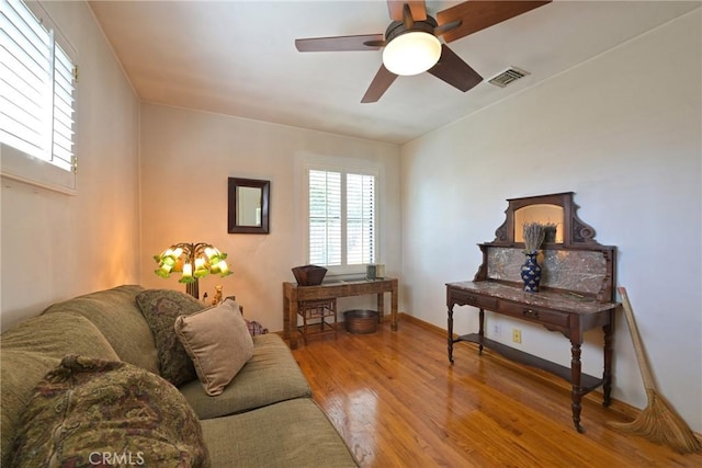 living area with baseboards, wood finished floors, visible vents, and a ceiling fan