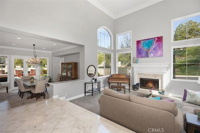 living area featuring marble finish floor, a towering ceiling, ornamental molding, a chandelier, and baseboards