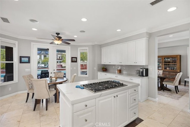 kitchen with tasteful backsplash, visible vents, light countertops, crown molding, and stainless steel gas cooktop